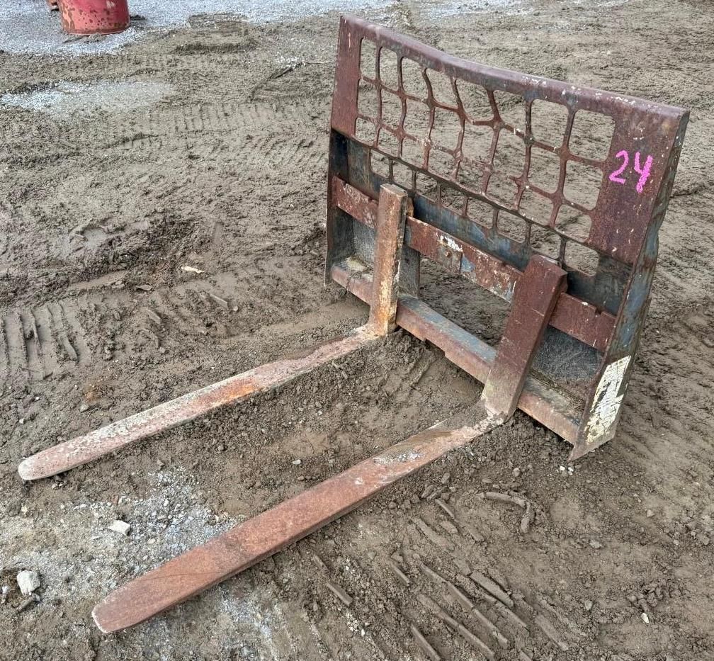 metal pallet jack forks on ground with a brick-patterned backplate marked “24”