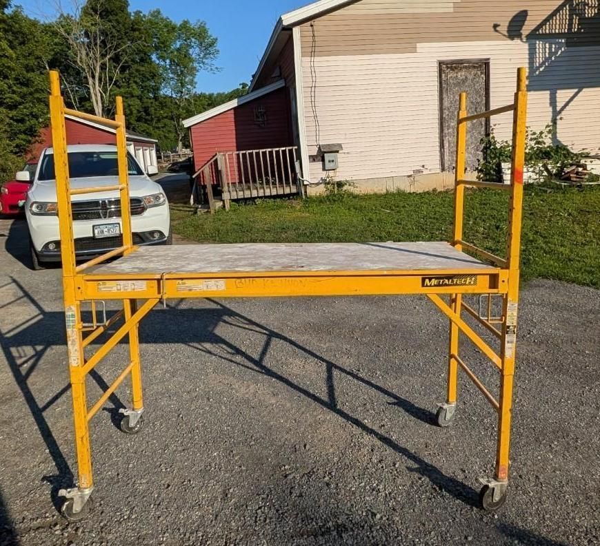 Yellow rolling scaffold on asphalt driveway outside a house
