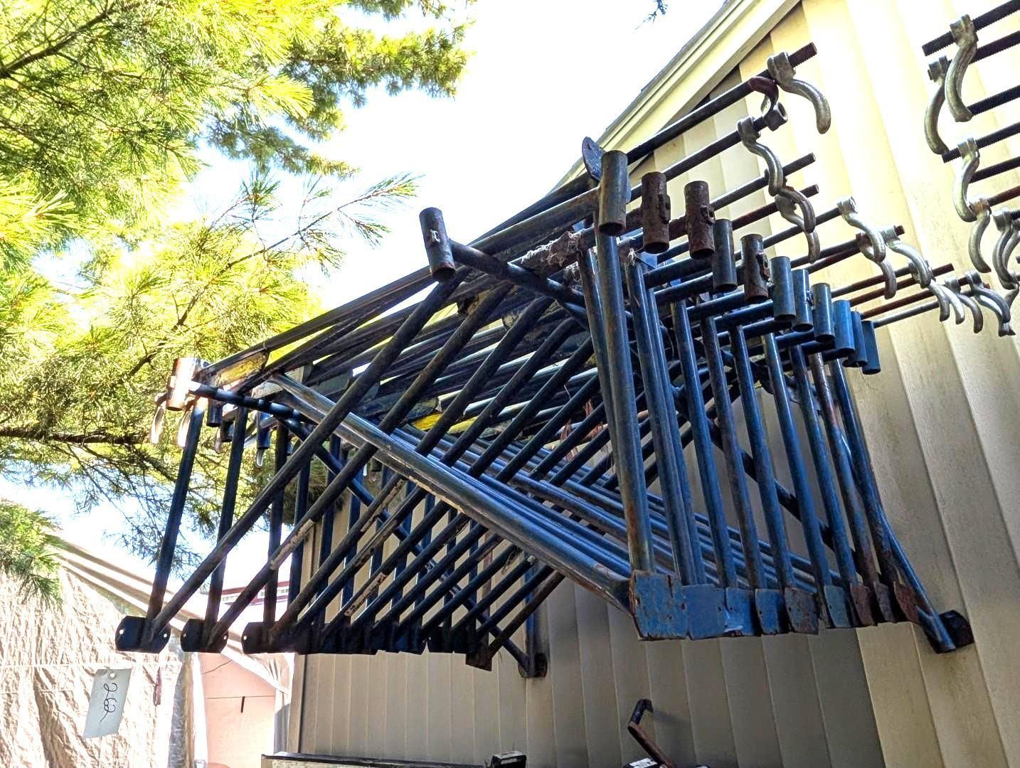 Blue stacked scaffolding stored on a wall-mounted rack outdoors under trees