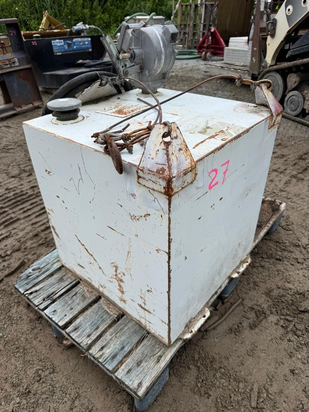 white metal tank on a pallet in a yard with machinery in the background