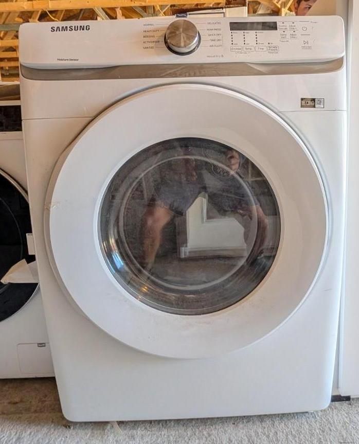 White Samsung front-load dryer in a laundry room with a round glass door and top control dial