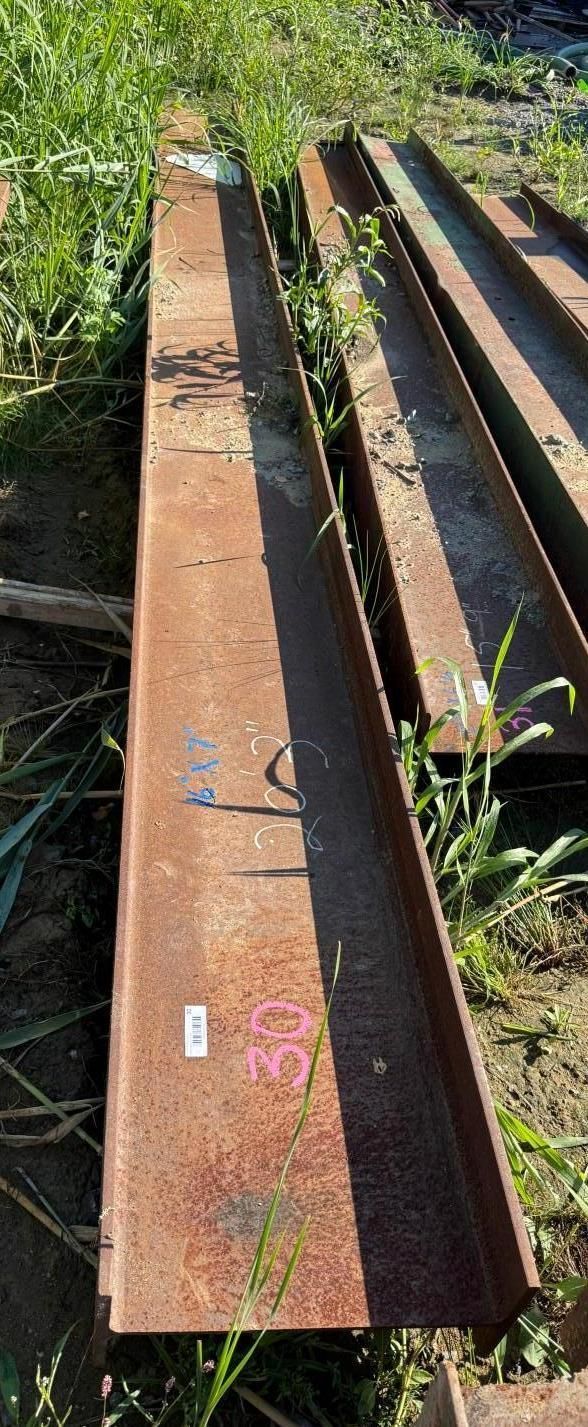 steel beams and long metal rails stacked outdoors in overgrown grass
