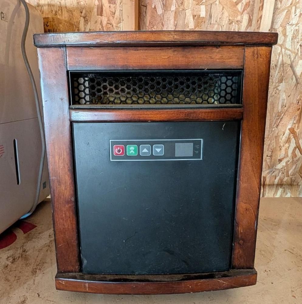 Wooden-framed black heater with honeycomb vent, standing on a plywood floor
