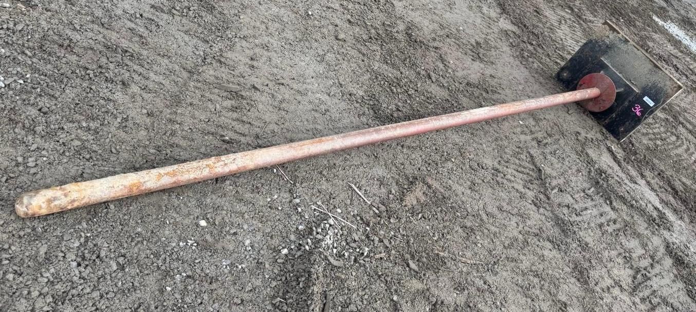 A long-handled hoe with a black head lying on gray gravel.