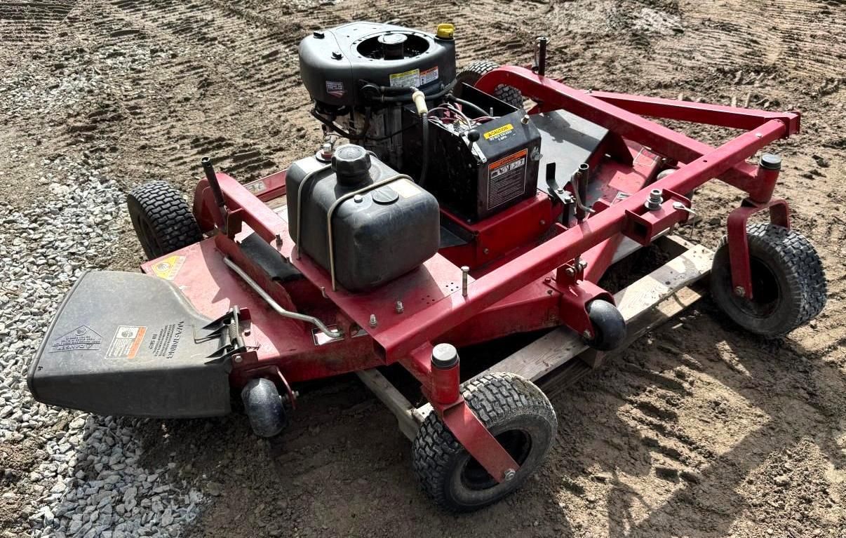 Red lawn mower on dirt, with black engine and front deck attached to a red metal frame.