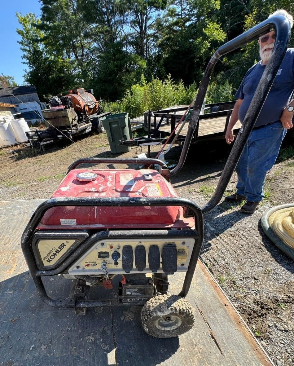 red portable generator on a gravel driveway with trees and equipment in the background