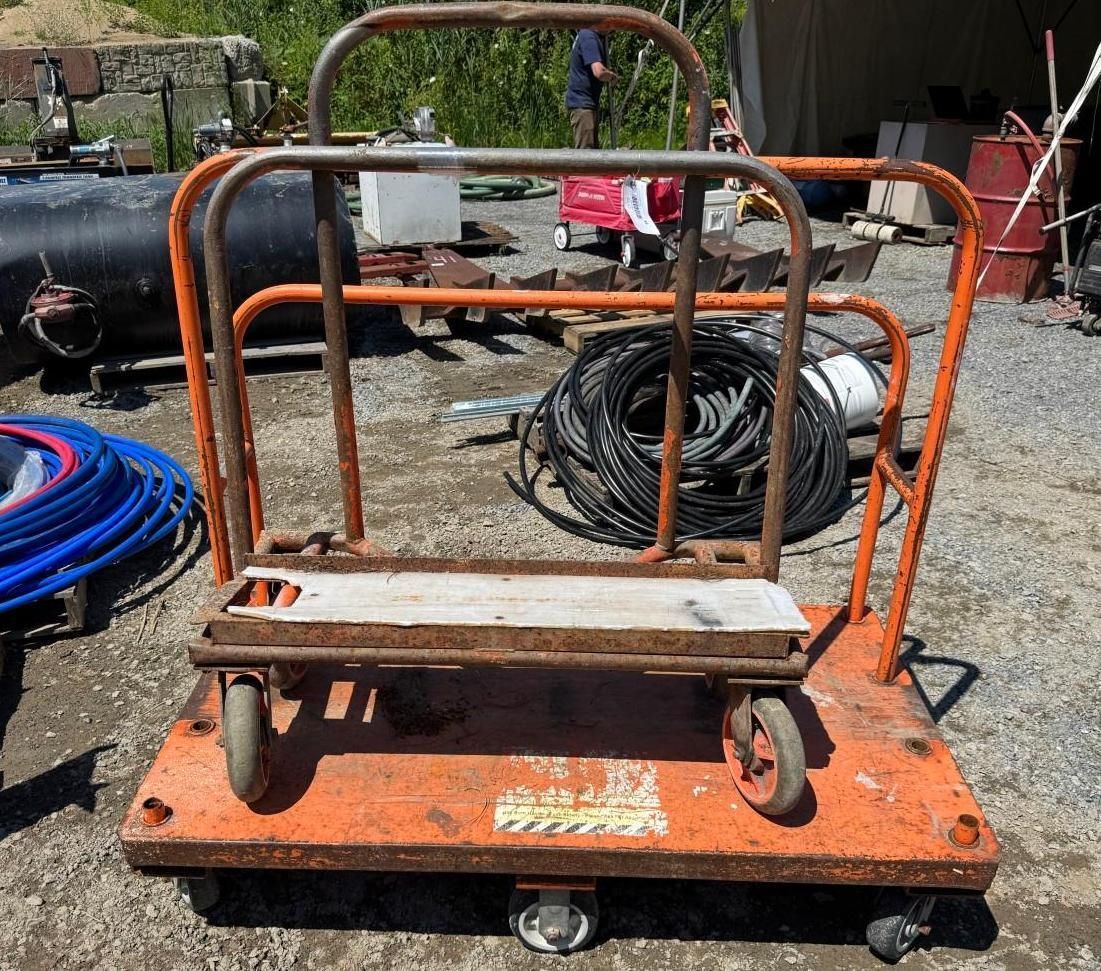 Orange flatbed cart with metal railings and wheels in an outdoor work yard