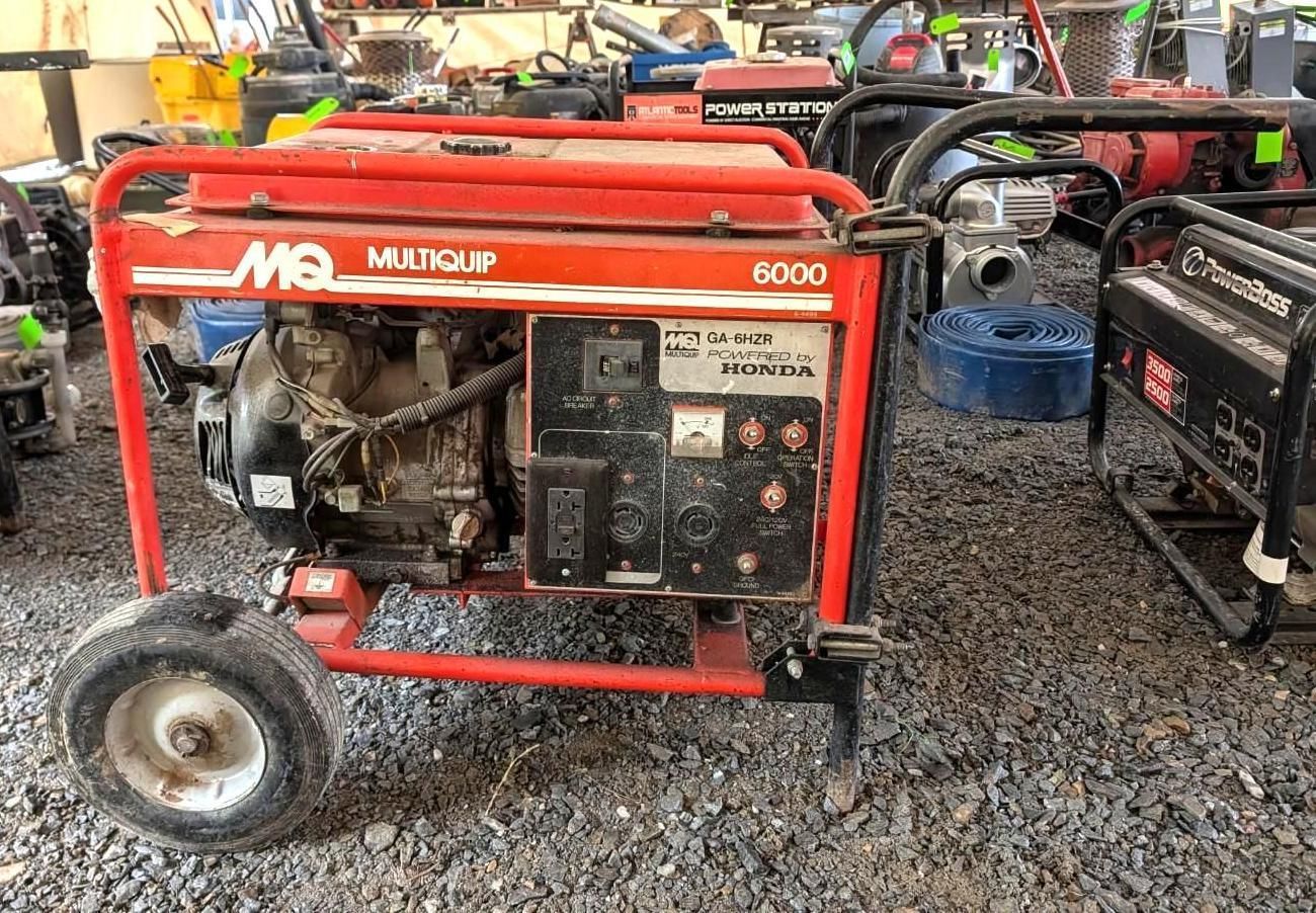 Red portable generator on gravel at an outdoor equipment lot, with other machines in the background