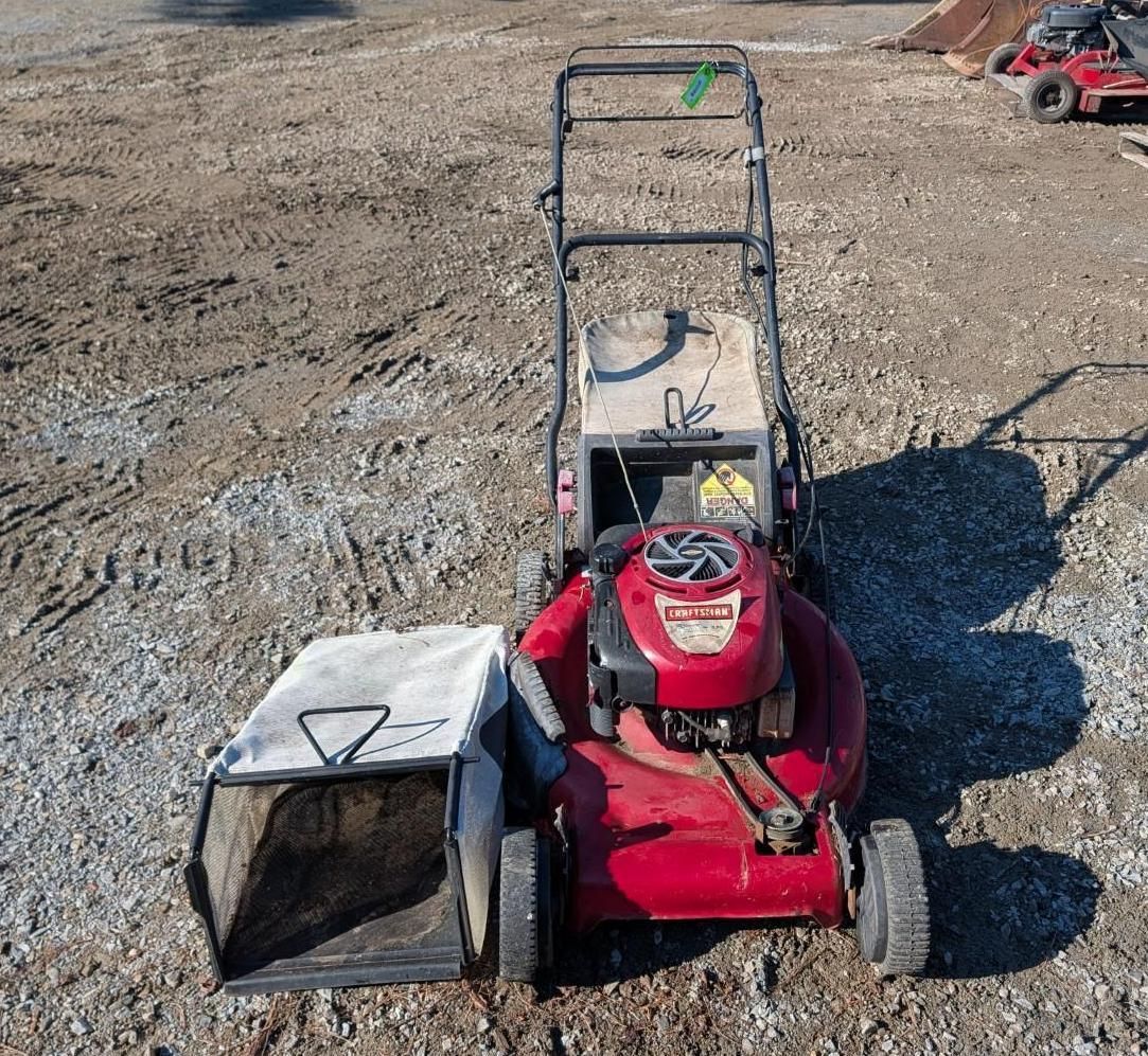 Red riding lawn mower with a white bagger attachment on a gravel lot, near a dirt road.