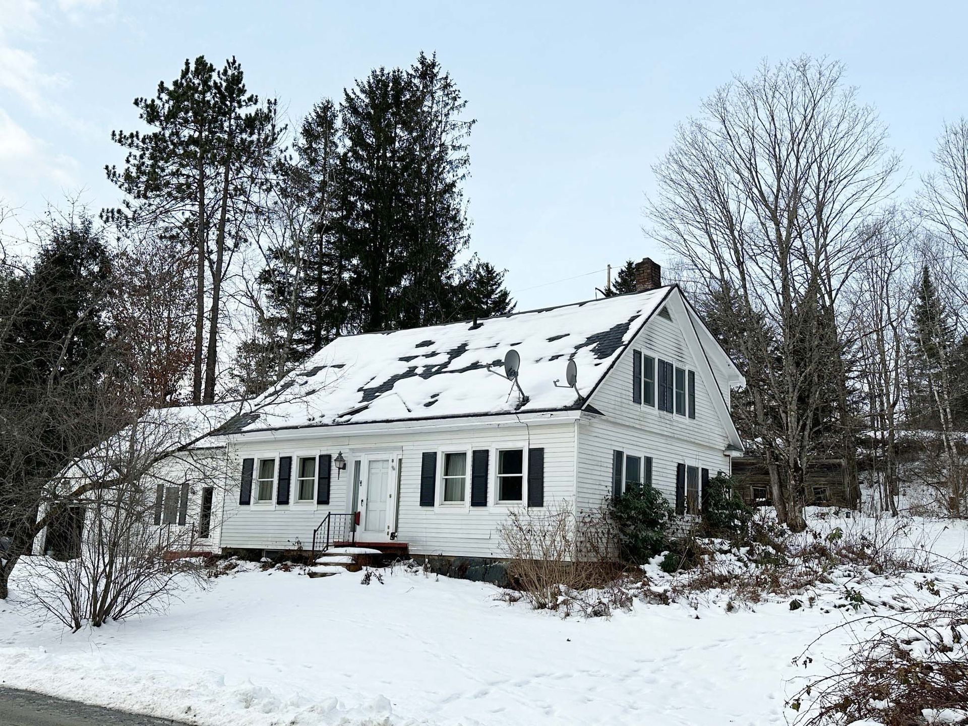 White house with snow-covered roof, surrounded by snow-covered ground and bare trees.