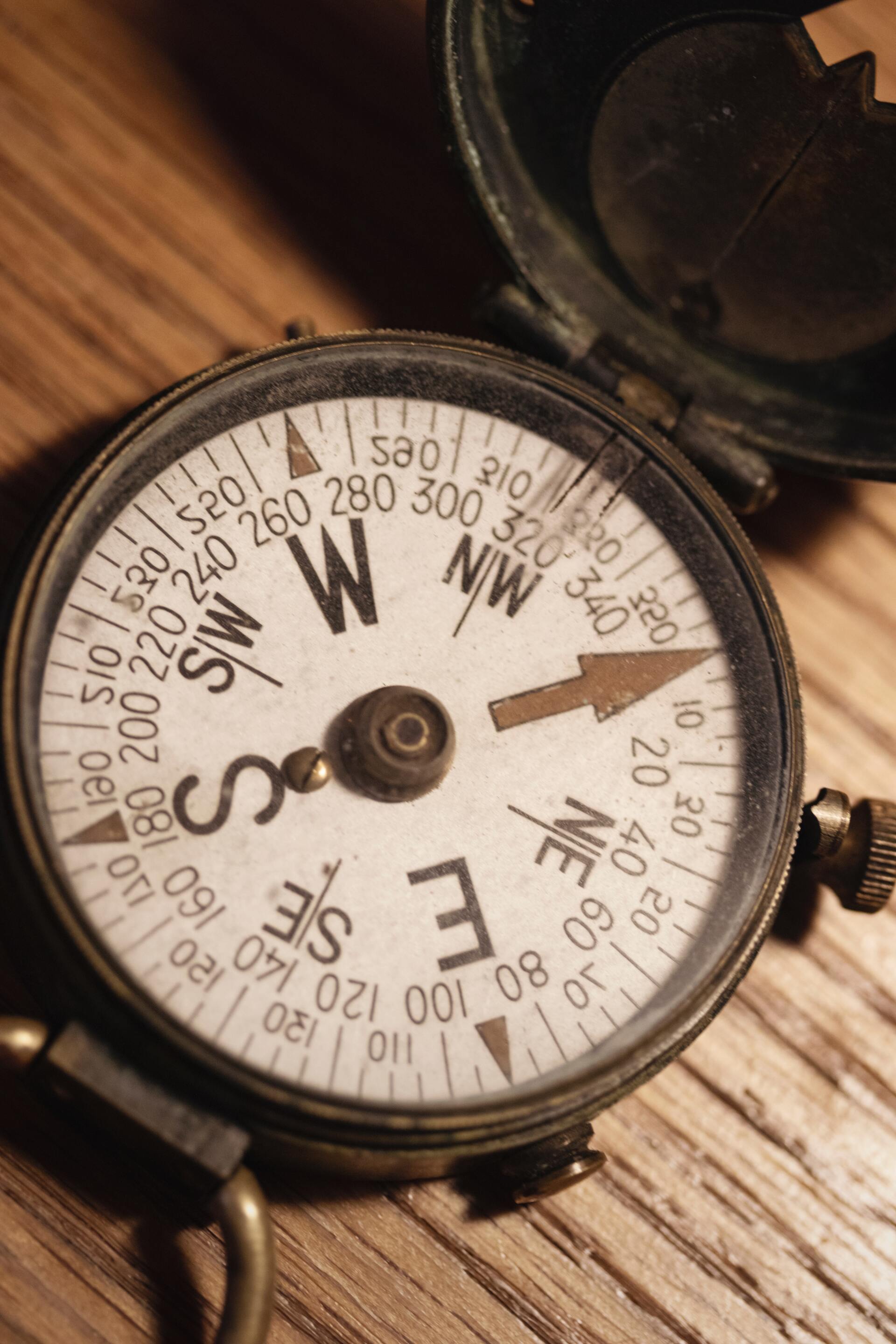 Close-up of an old compass on wood, showing direction markings: N, S, E, W, and degrees.