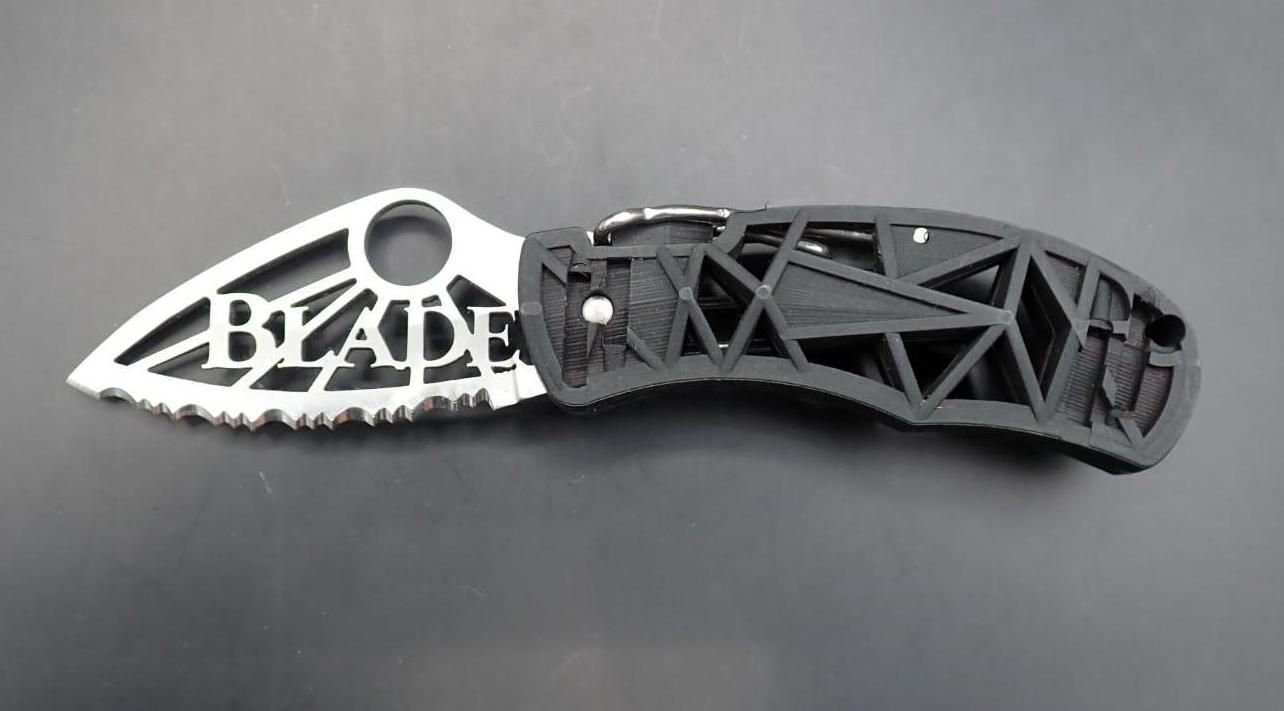 Black folding knife with silver “BLADE” cutout handle on a gray background