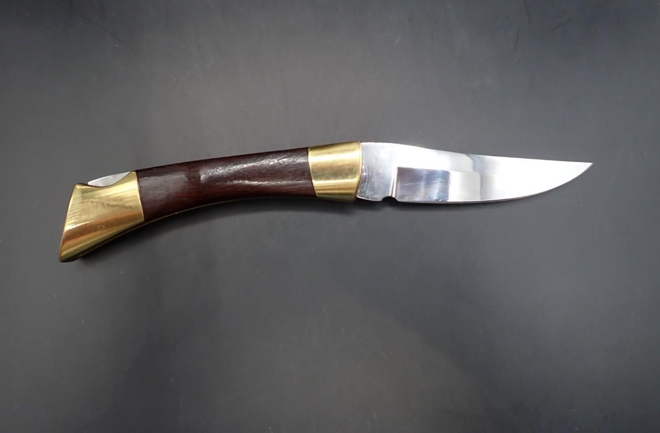 Curved folding knife with dark wood handle, brass accents, and a silver blade on a black background