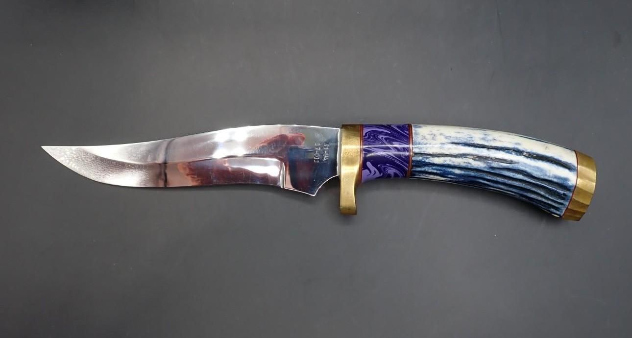 Curved knife with a patterned blue handle and brass guard on a gray background