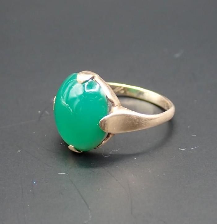 Gold ring with a large green oval gemstone on a dark background