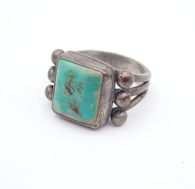 Silver ring with a turquoise square stone and decorative bead accents on a white background