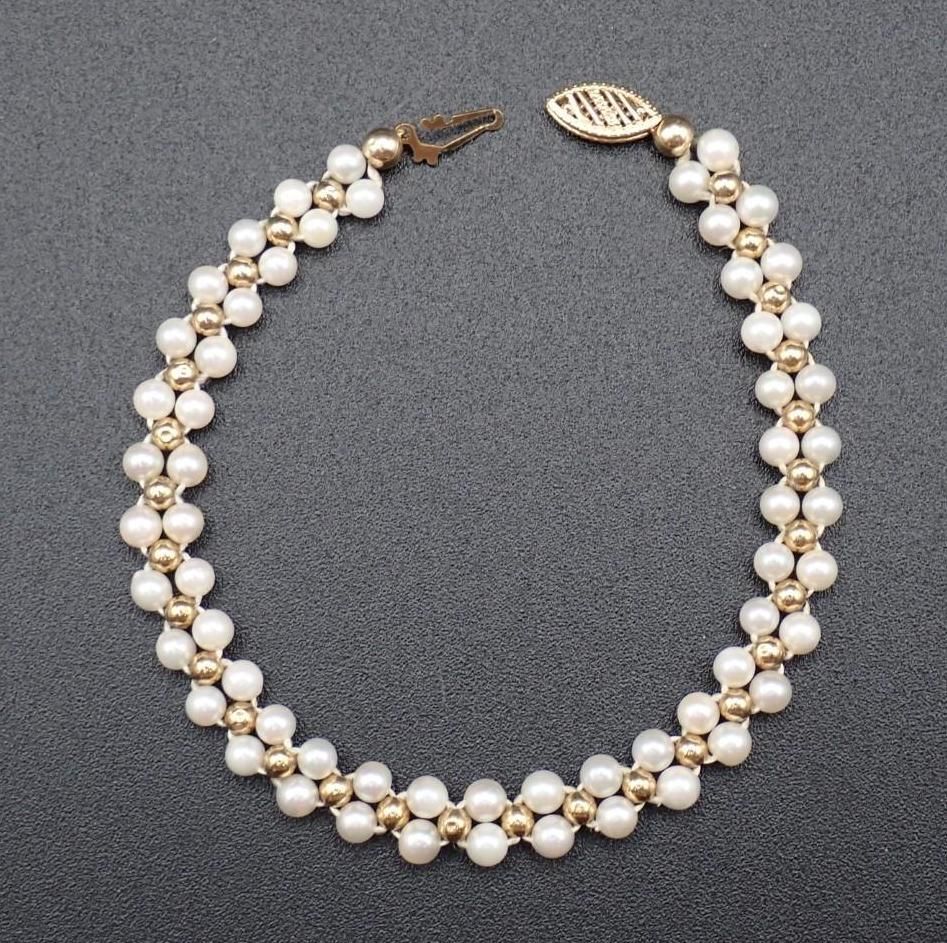 Pearl and gold beaded necklace with a leaf-shaped clasp on a gray background