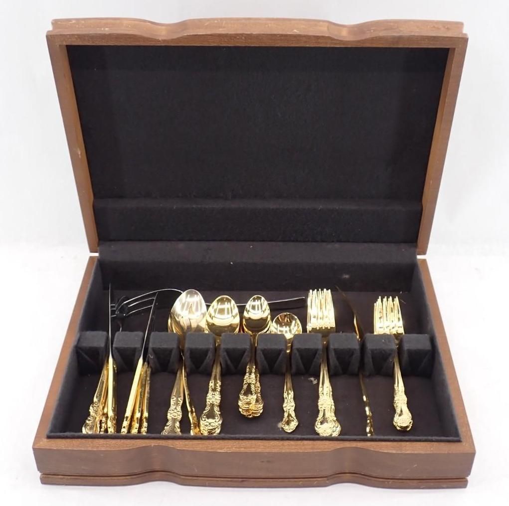 Open wooden presentation box with gold-colored cutlery arranged in rows on black lining