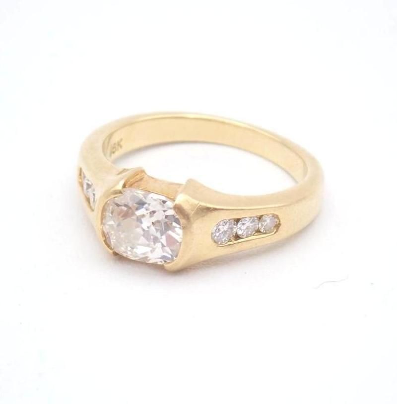 Gold ring with a large round clear gemstone and small side stones on a white background