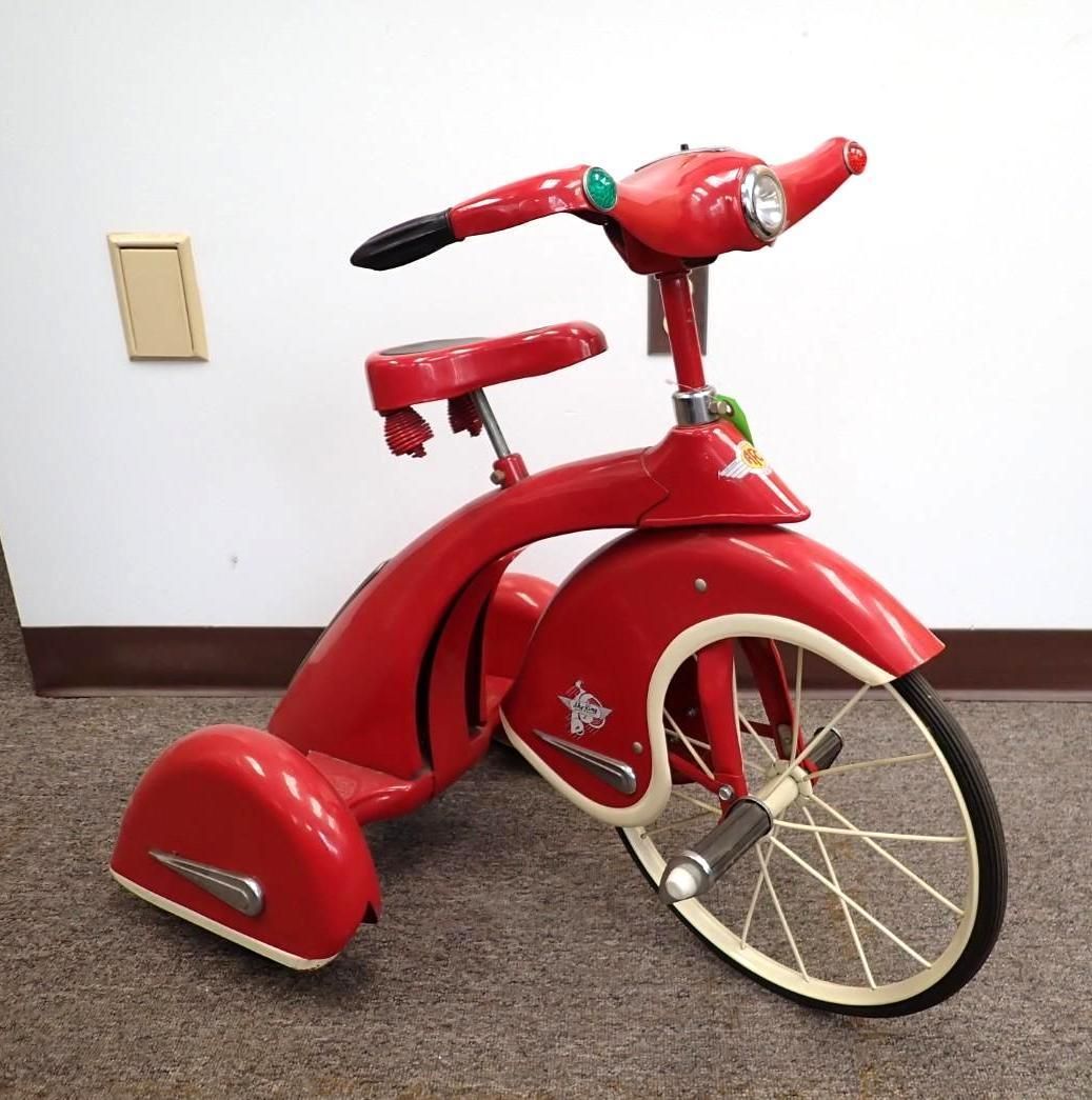 Red child’s tricycle with a canopy and training wheels against a white wall