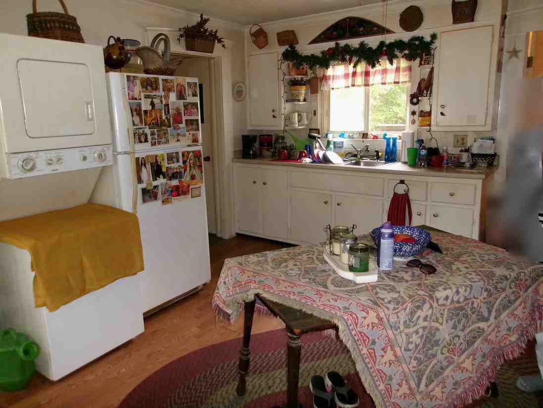 Cozy kitchen with white cabinets, refrigerator, and a table covered in a patterned cloth by a window.