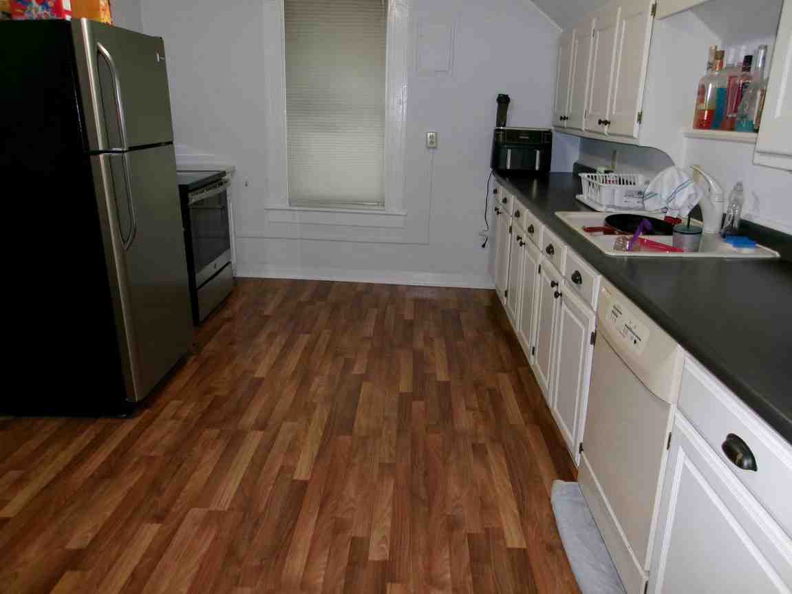 Empty kitchen with dark cabinets, black appliances, and wood-pattern flooring.