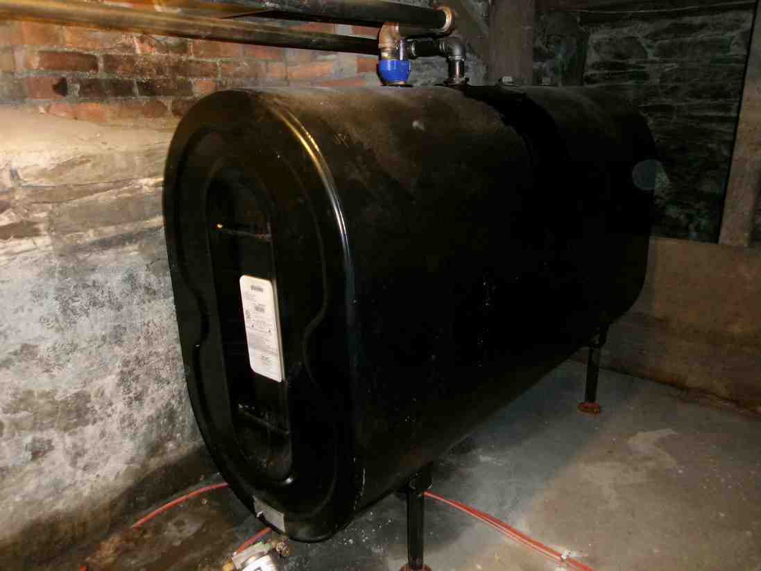 Large black cylindrical tank in a basement, with pipes running above it and a concrete floor below.