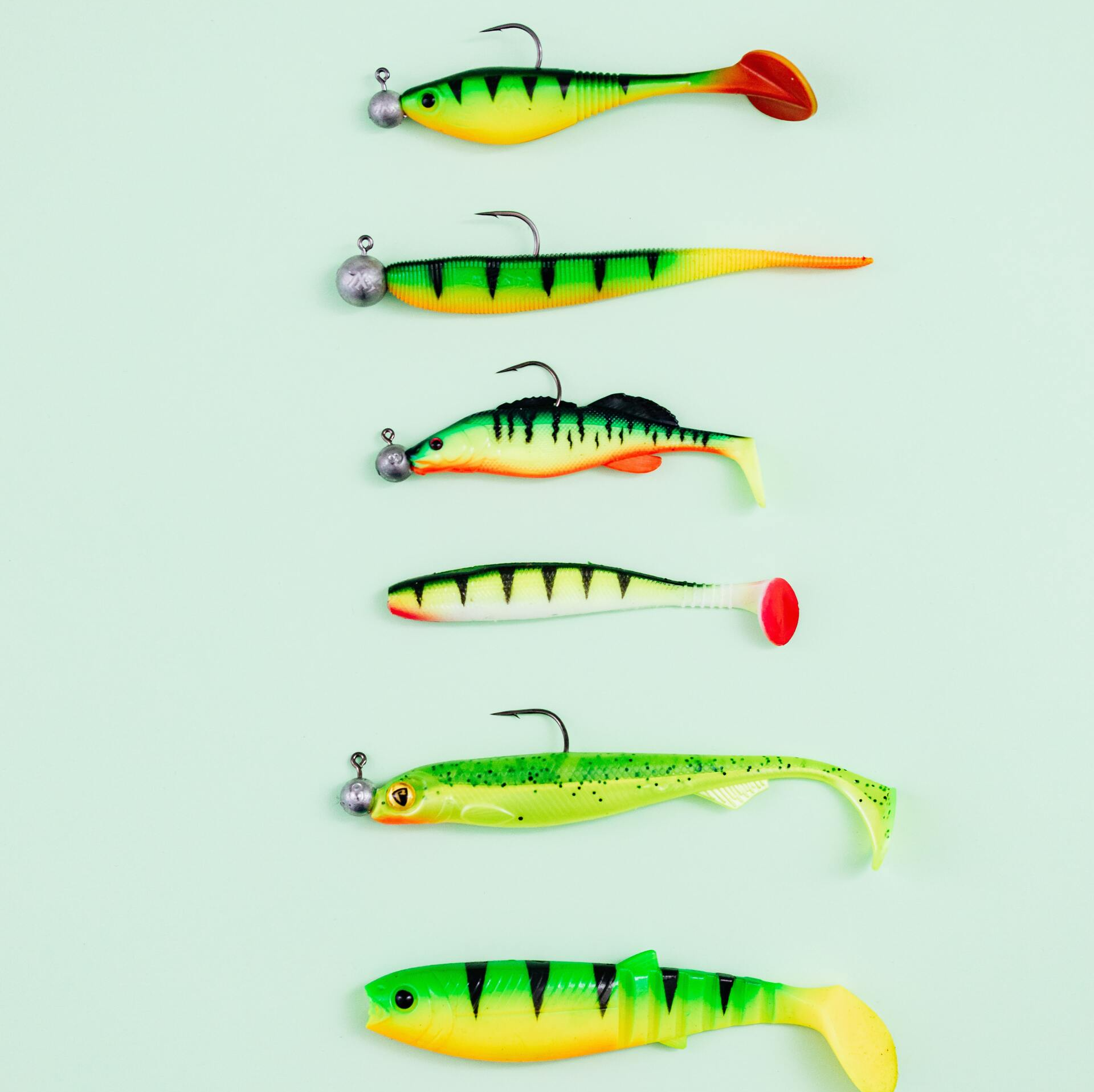 Six colorful plastic fishing lures arranged on a light blue background.