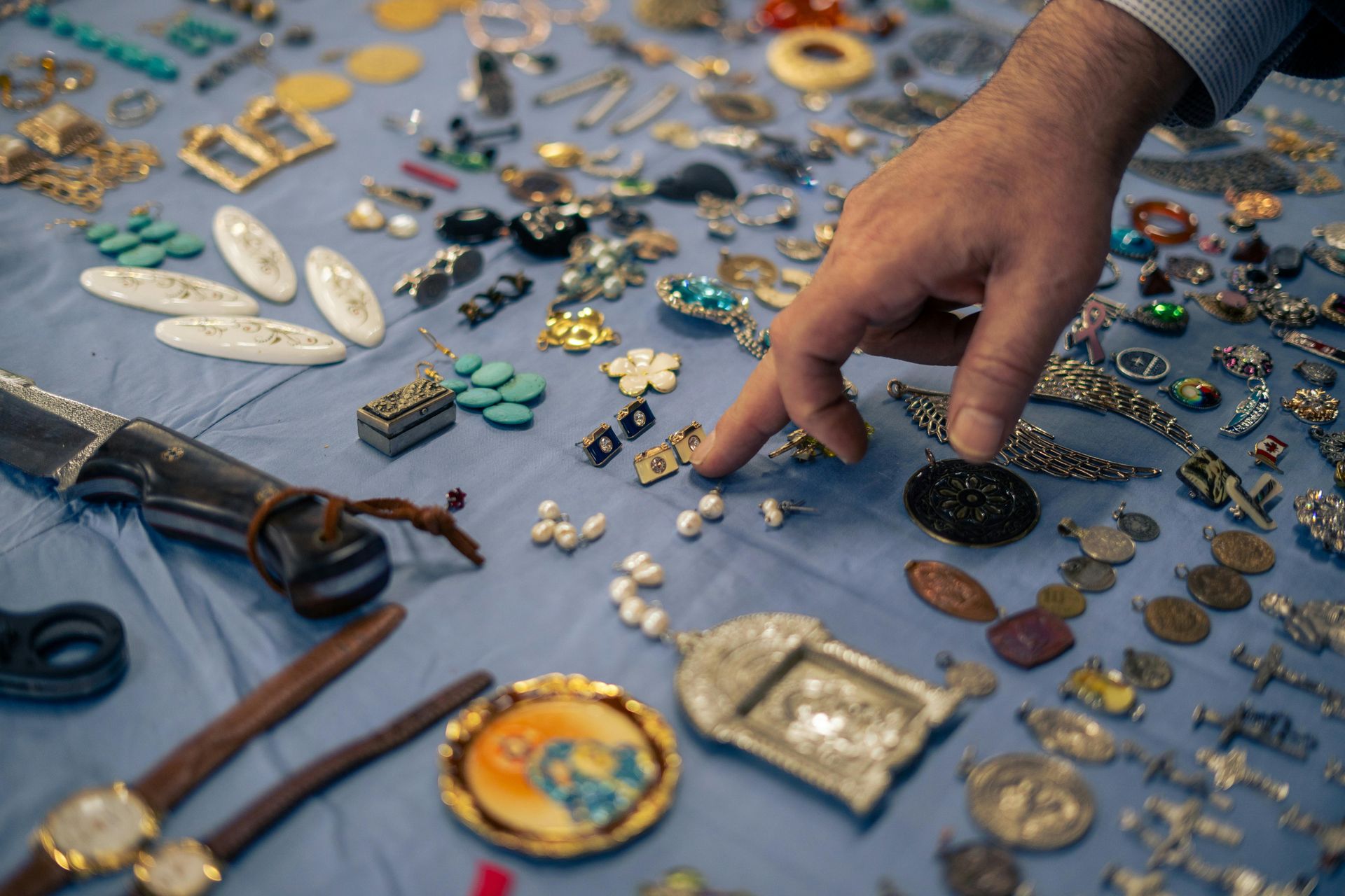 Hand reaching over assorted vintage jewelry and brooches laid out on a blue cloth at a market stall