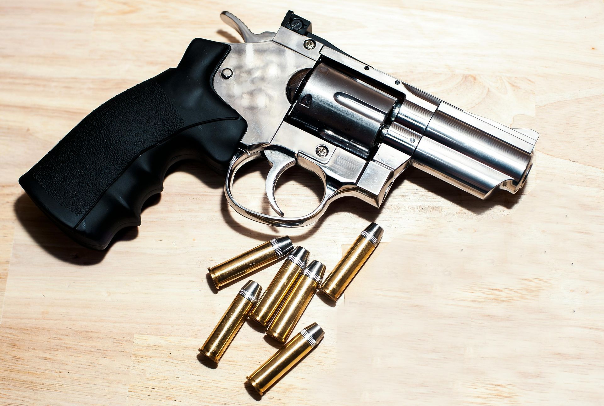 Silver revolver with black grip and several bullets on a light wooden surface