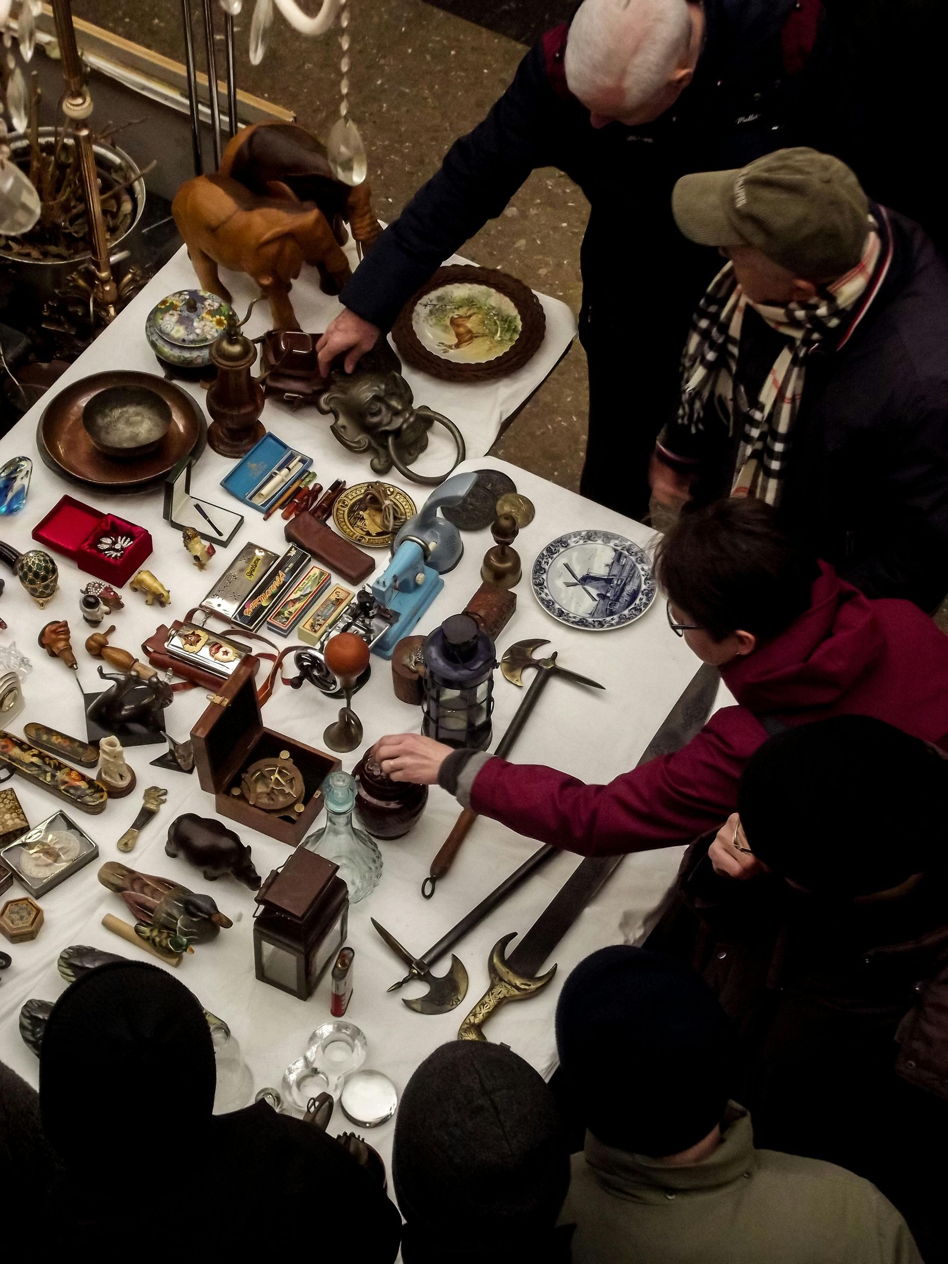 People browsing a crowded market table filled with antiques, jewelry, and small decorative items