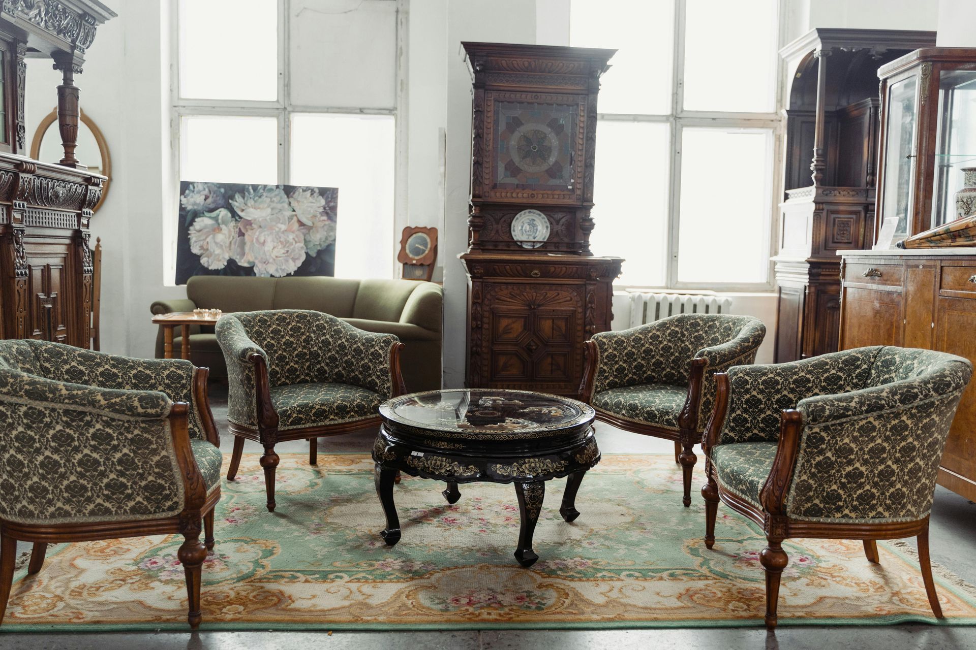 Vintage living room with upholstered chairs, ornate table, clock cabinet, and large windows