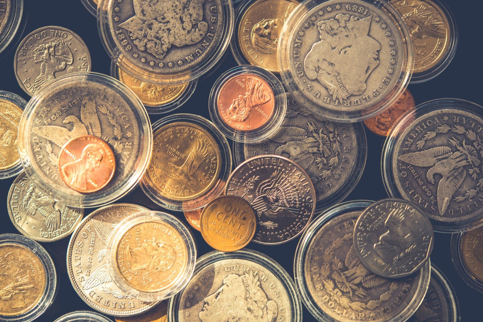 Close-up of assorted coins in protective cases, various sizes and colors, on a dark surface.