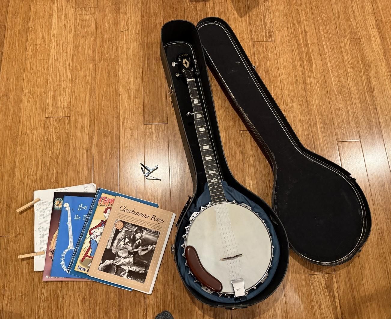 Banjo in open case next to music books on wooden floor.