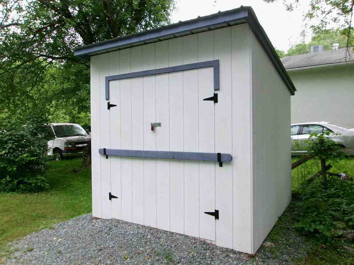 White garden shed with a front door and dark trim on a gravel yard