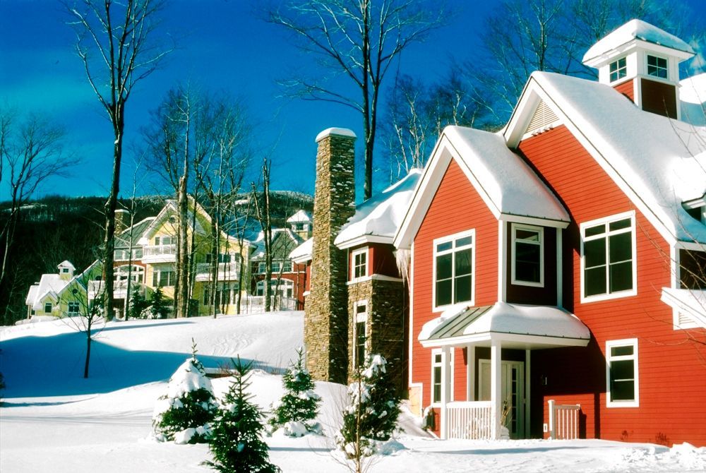 Red and yellow houses with snow-covered roofs in a snowy mountain setting under a clear blue sky.