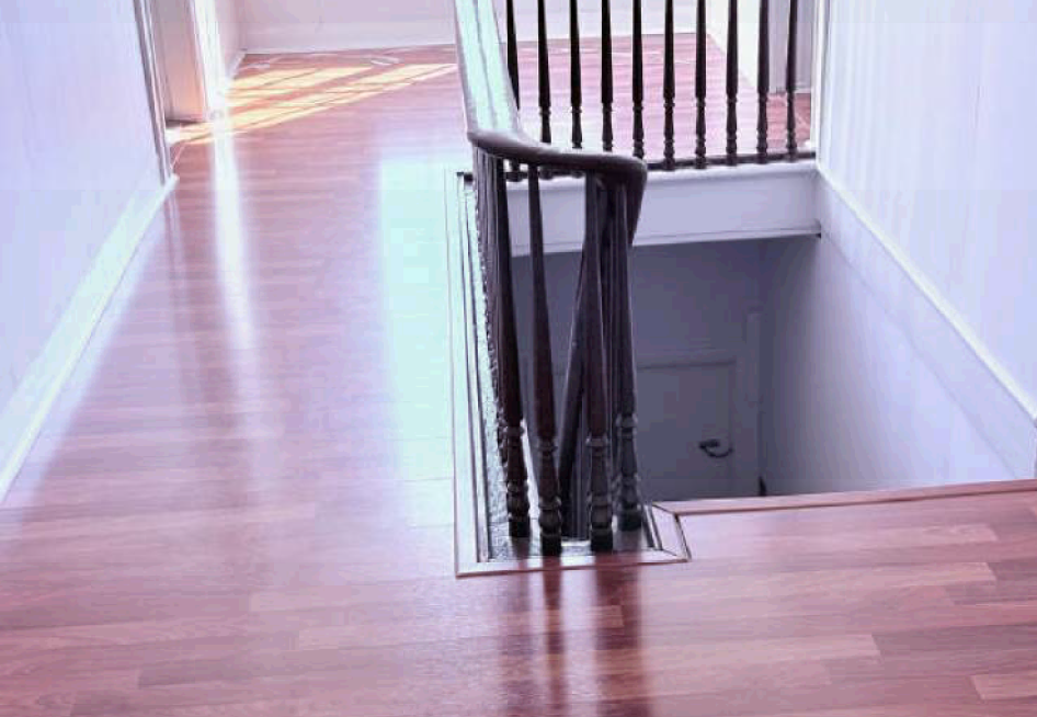 Hallway with wooden floors and an open stairwell with dark railings and white walls