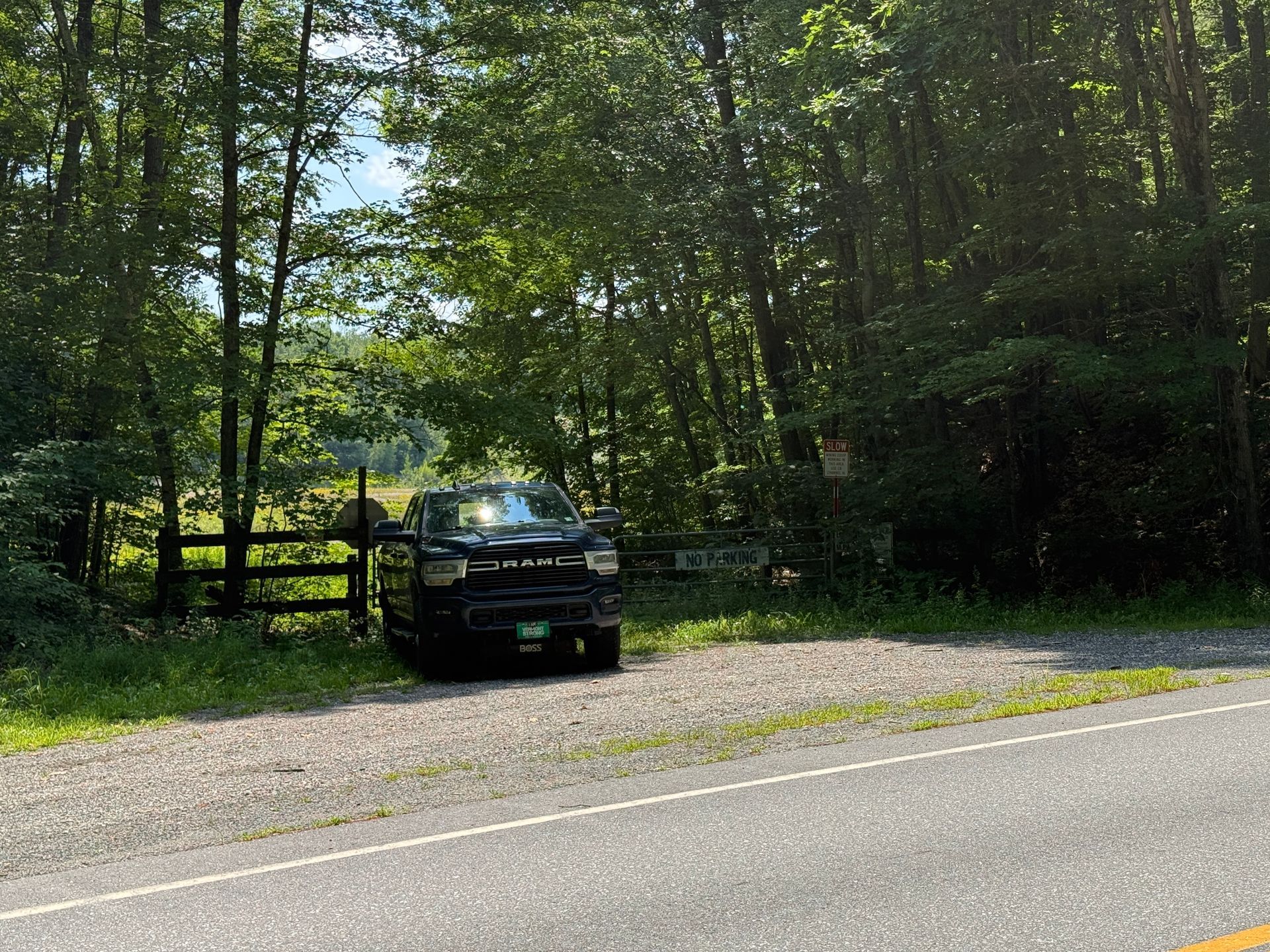 Black SUV parked by a wooden gate on a gravel pull-off beside a wooded roadside