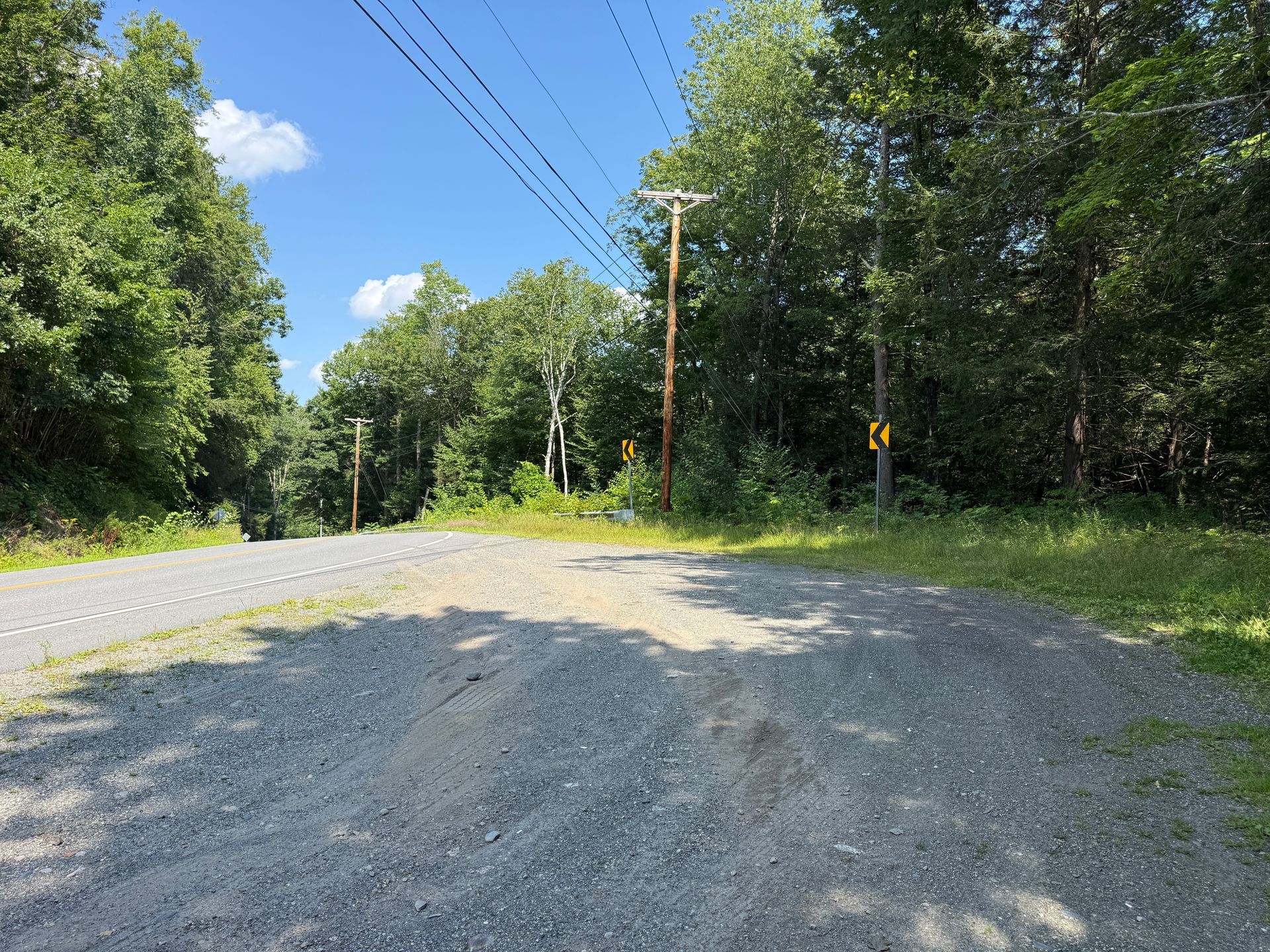 Gravel road curving through a wooded area under a blue sky with power lines overhead