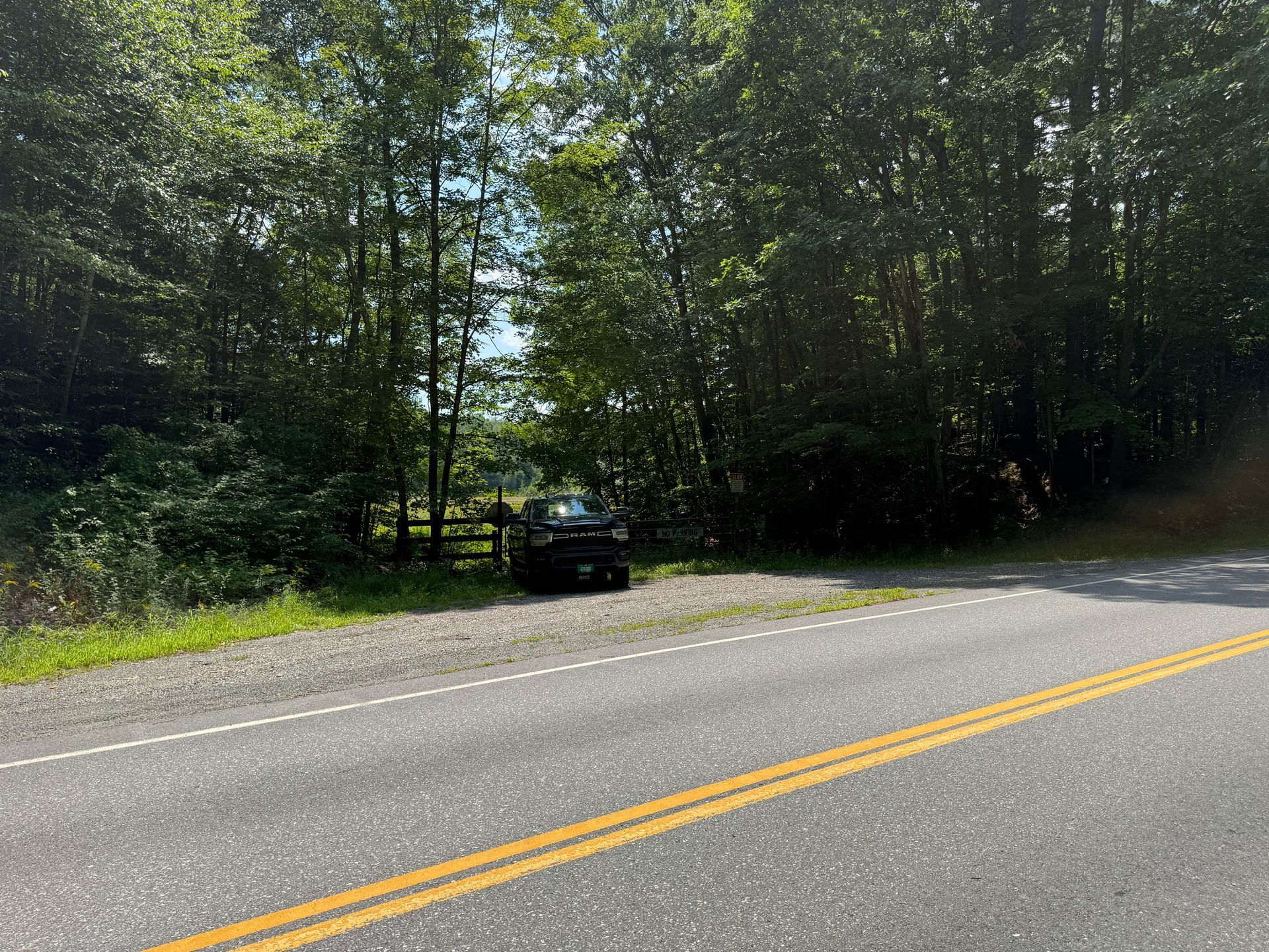 Car stopped at the edge of a wooded roadside beside a two-lane road with double yellow lines.