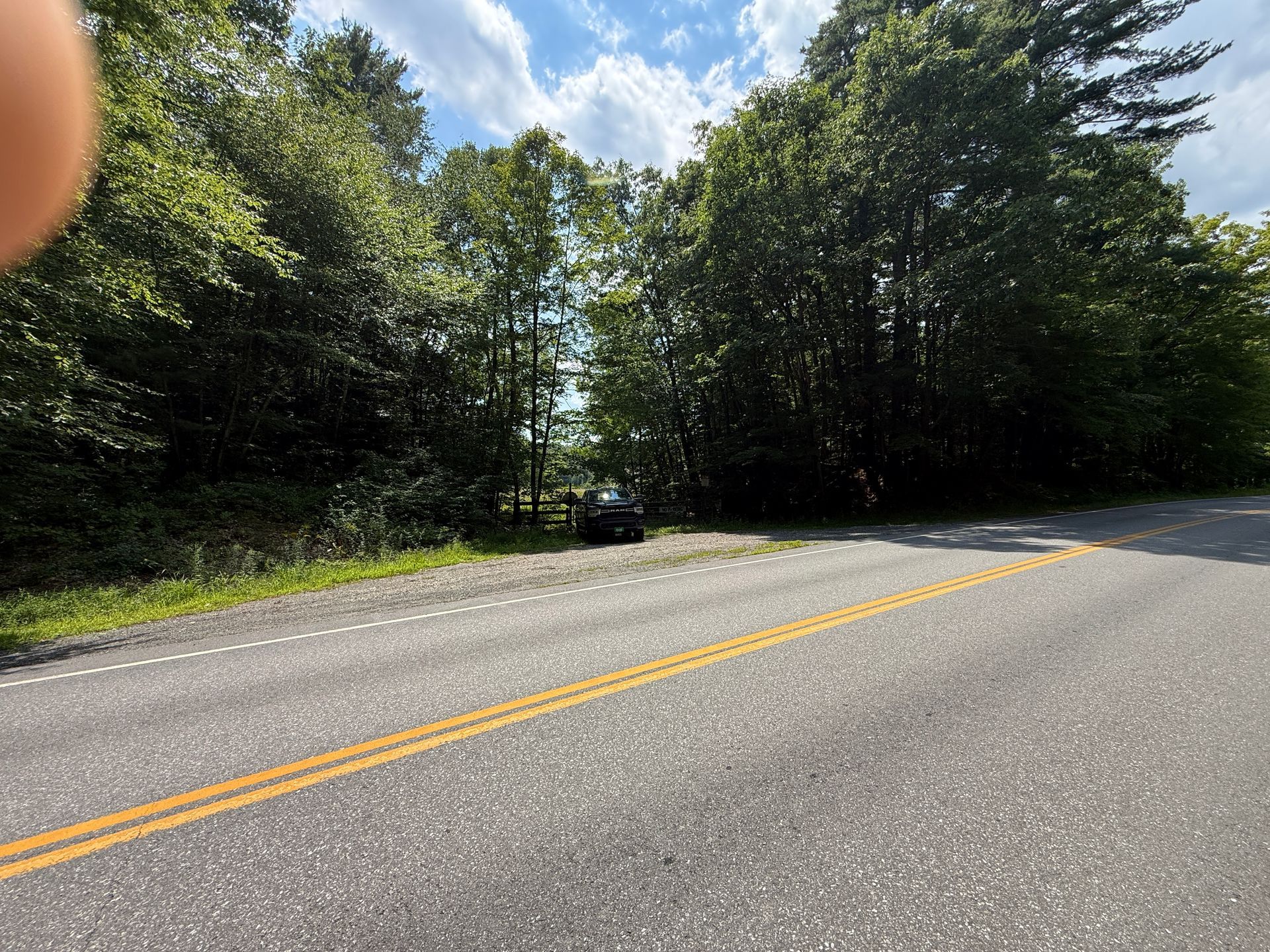 Empty two-lane road beside dense green trees under a partly cloudy sky