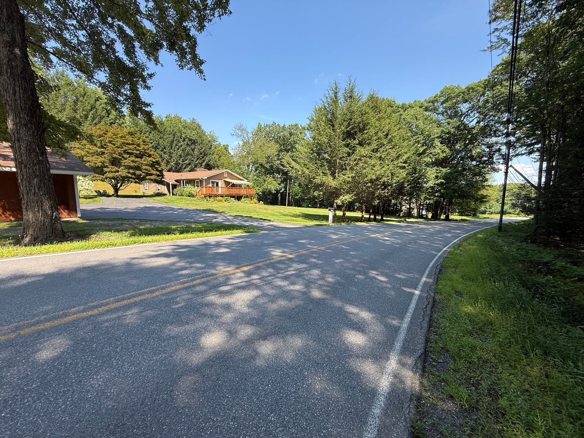 Curving paved road through a sunny green park with trees and a house in the distance