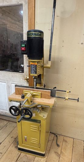 Yellow vertical metal lathe in a workshop, with handwheels, control panel, and black motor above it.