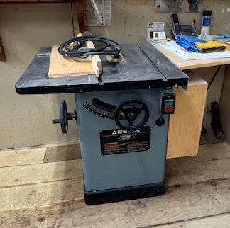 Table saw in a workshop with a wood board and coiled cord on top.