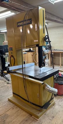 Wooden bandsaw in a workshop, with black metal cutting table and tall yellow frame.