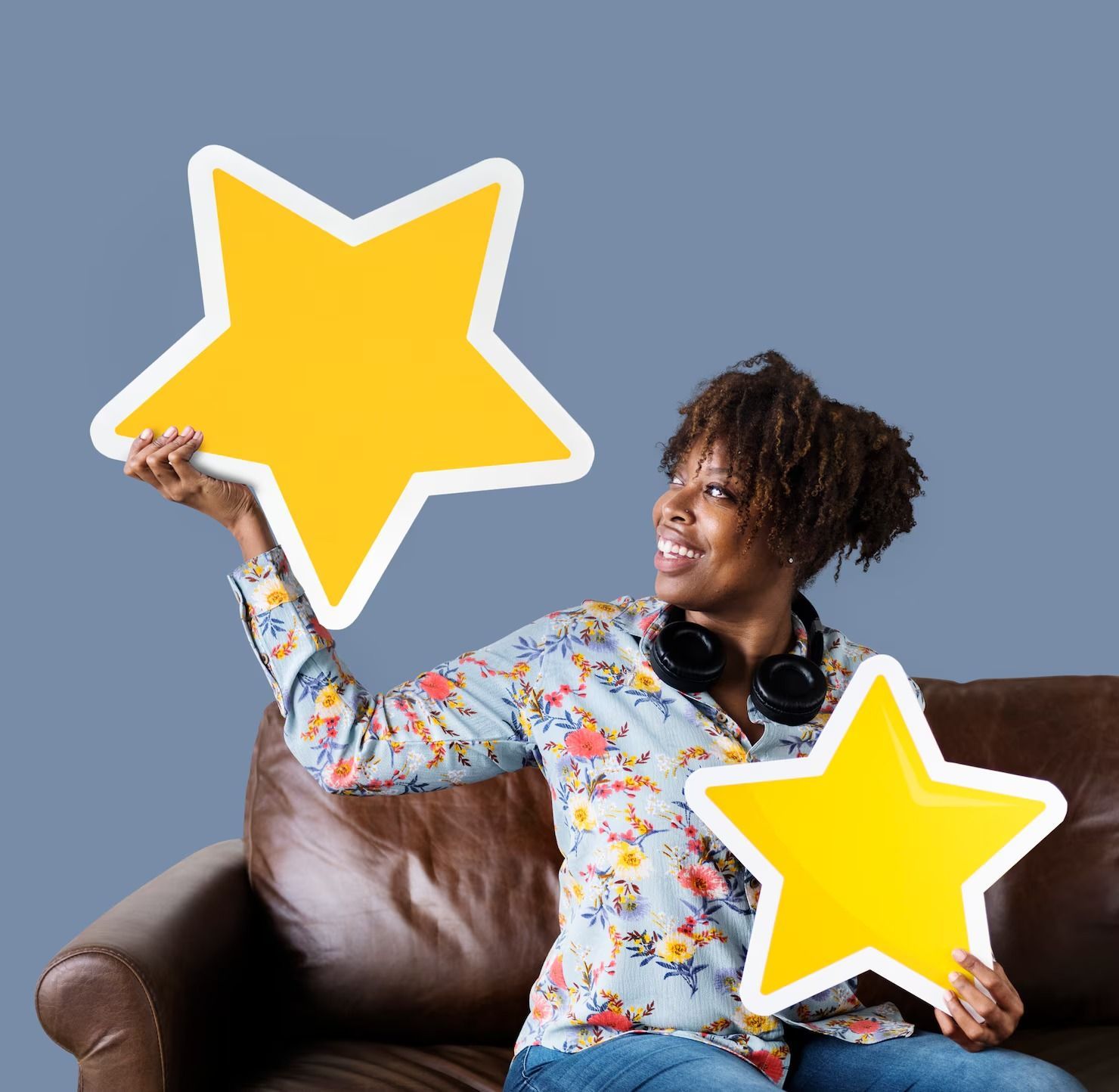 Femme tenant des étoiles jaunes découpées, souriante, assise sur un canapé marron.