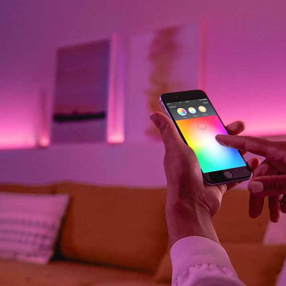 Une personne utilise son téléphone pour contrôler des lumières intelligentes colorées qui illuminent une pièce.