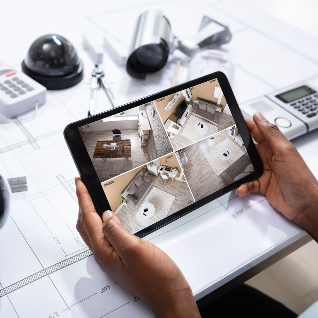 Une personne tenant une tablette affichant les images de plusieurs caméras de sécurité est entourée d'équipements