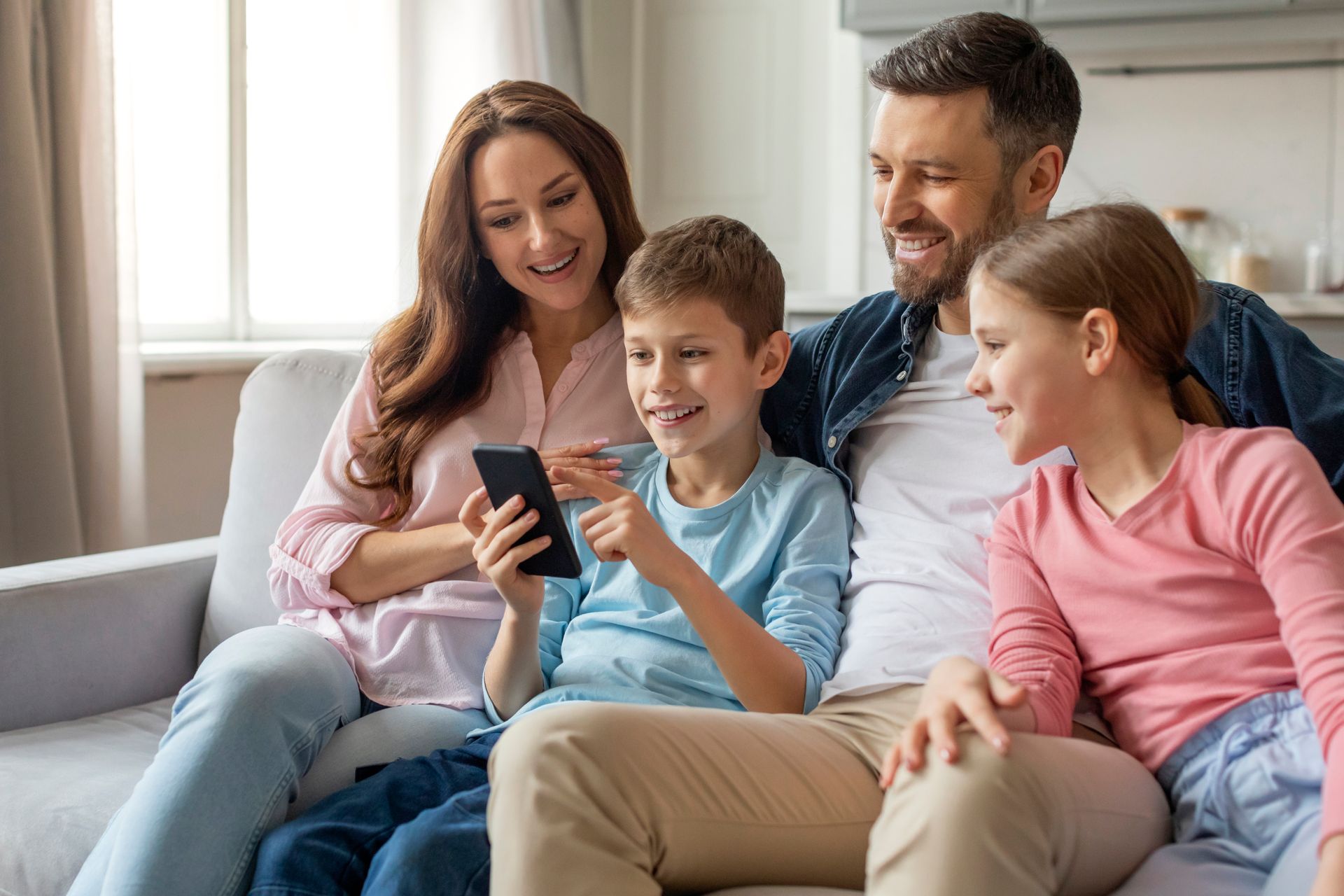 Family sitting on a couch, smiling as they look at a smartphone together.