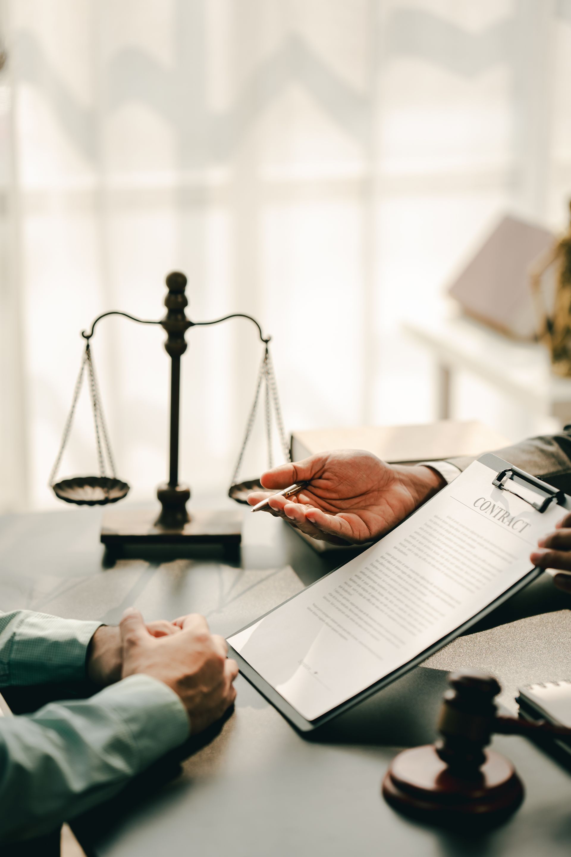 Legal consultation with scales of justice, a clipboard, and hands reviewing documents at a desk.